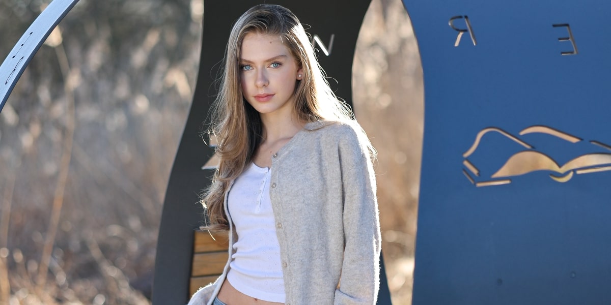 A young woman with long hair in a cardigan poses against a backdrop of modern geometric shapes, exuding a polished aesthetic.