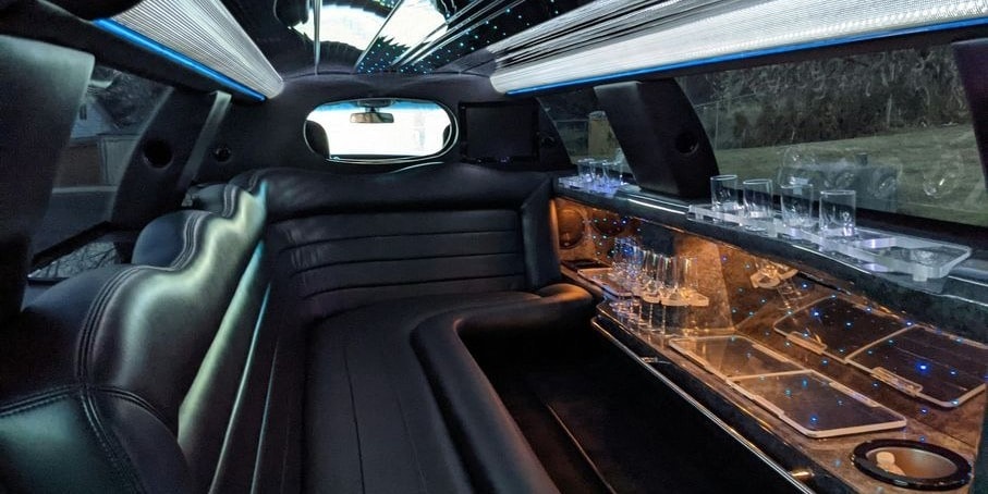 Interior of a luxury limousine featuring sleek leather seating, ambient lighting, and glassware along the bar area.