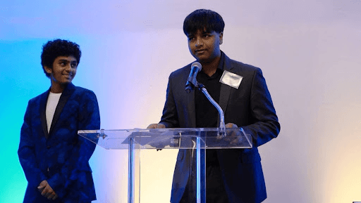 Two students accept an award for their mobile app, "Home Of My Own," addressing homelessness education through technology.