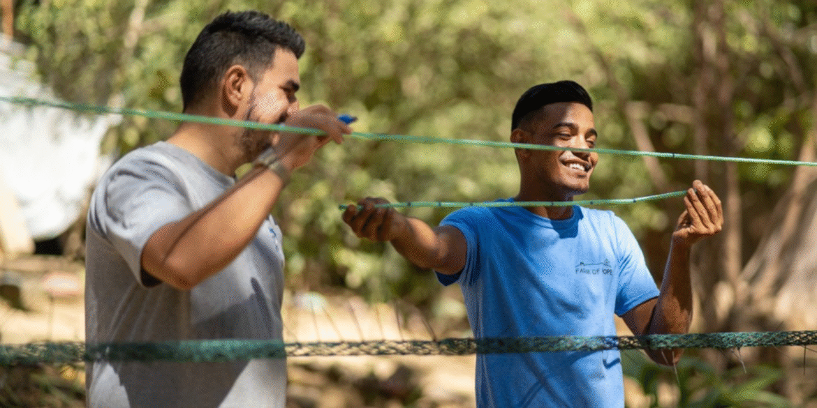 Two volunteers smiling while setting up netting outdoors at The Monkey Farm community project in Costa Rica.
