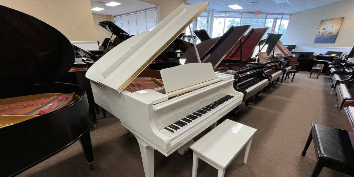 White Kawai grand piano on display in showroom surrounded by other grand pianos for sale.