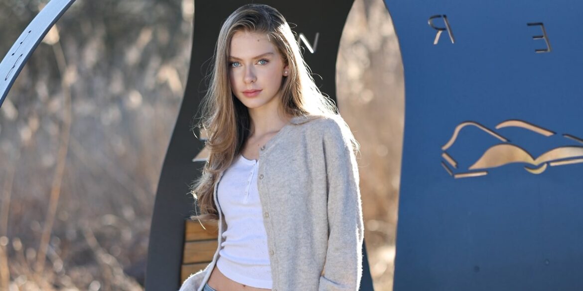 A young woman with long hair in a cardigan poses against a backdrop of modern geometric shapes, exuding a polished aesthetic.