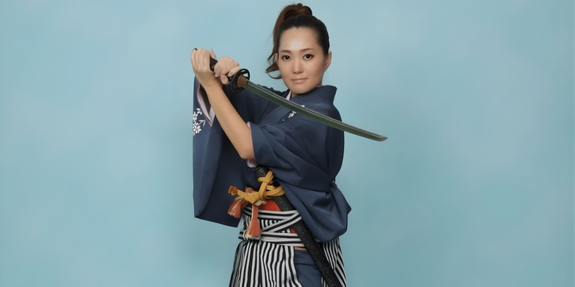 Woman in traditional attire holding a katana in poised stance against blue background