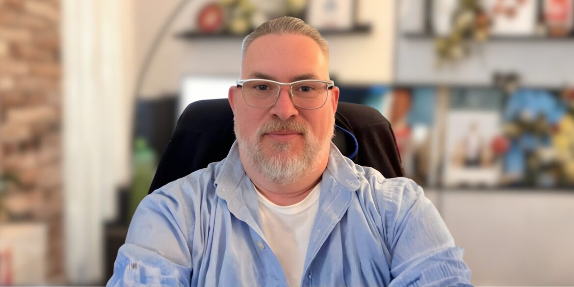 Micheal Franklin, a bespectacled man with a beard, sits in front of a computer, symbolizing his commitment to mental health counseling.