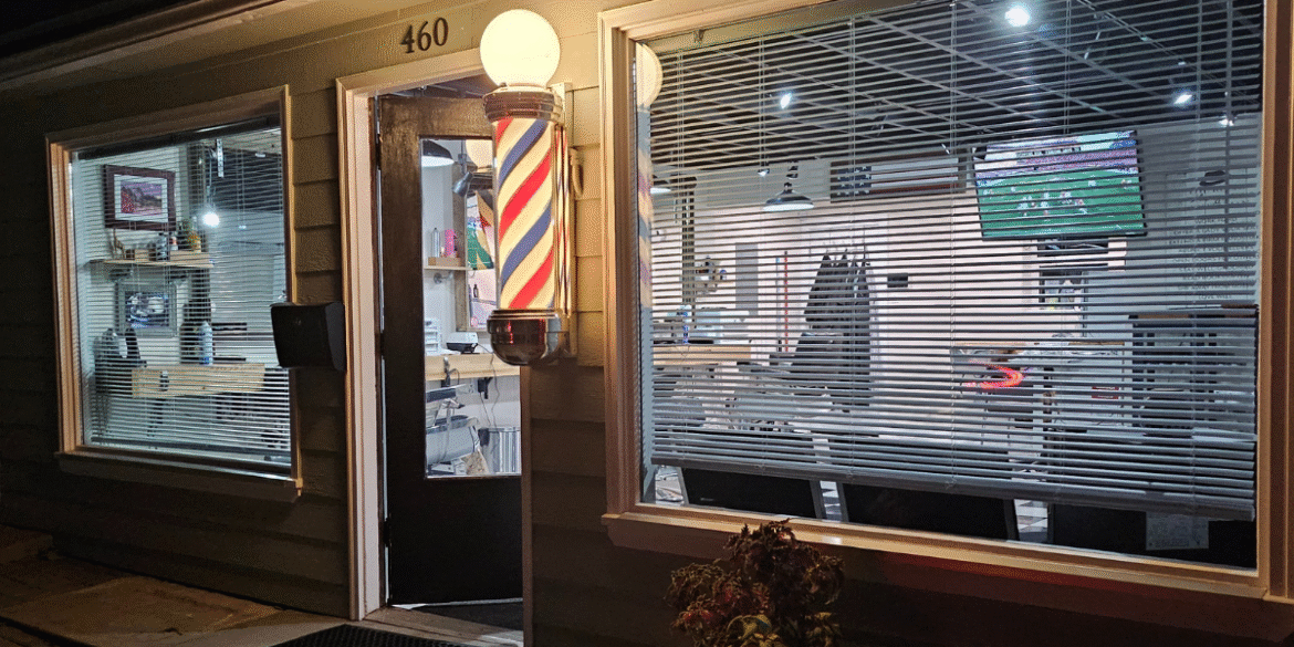 Exterior of Quincy Barbers with illuminated barber pole and storefront entrance at night.