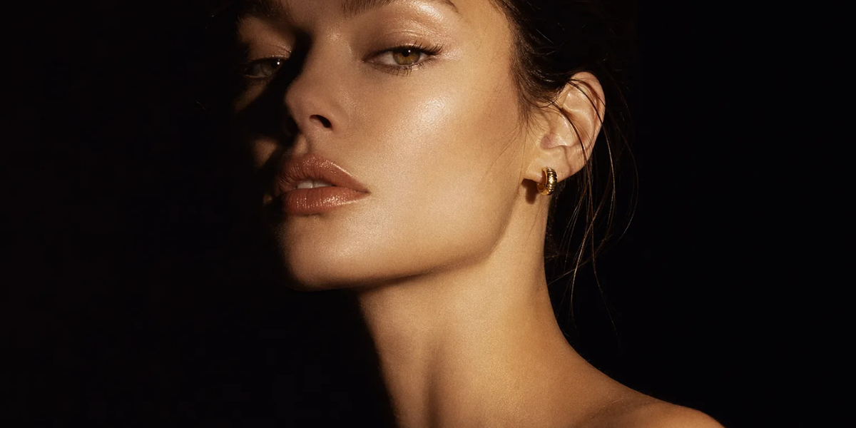 Close-up portrait of a woman with glowing skin wearing a gold hoop earring against a dark background.