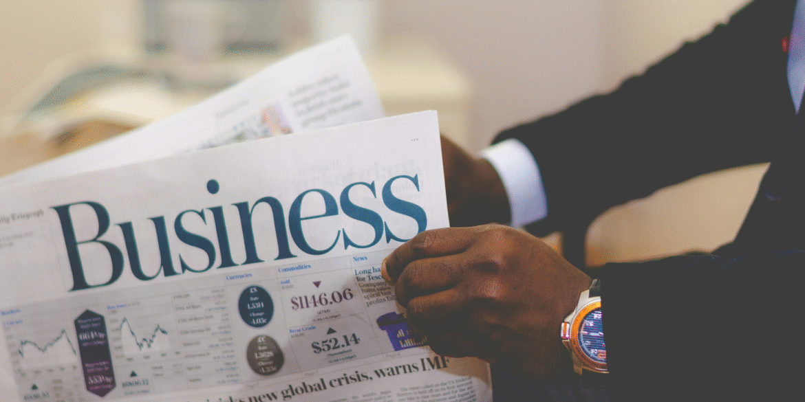 Person in business attire holding a newspaper with financial charts and market information.