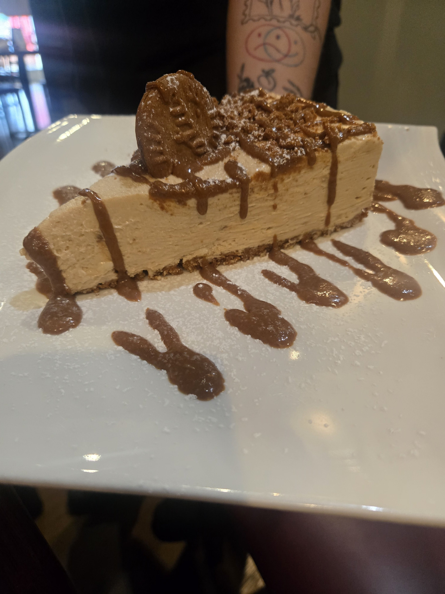 Slice of Italian cheesecake topped with cookie crumble and caramel drizzle on a white plate.